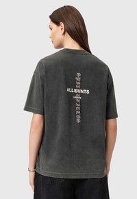 Grå bomulds t-shirt med korte ærmer. Har et lodret hvidt og pink logo print på ryggen. Casual, afslappet pasform.