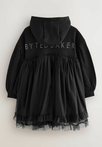 Černé šaty s kapucí, s vrchní částí ve stylu mikiny a nazbíranou tylovou sukní s volánkovým lemem. Na zádech nápis "BYTEDBAKER".