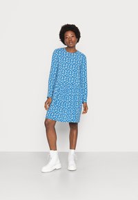 Vestido azul de mangas longas com padrão floral branco, cintura franzida e corte descontraído. Combinado com botins brancos de cadarço.