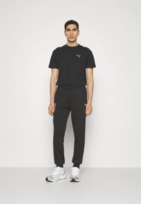 Sort kortærmet T-shirt med logo, kombineret med sorte joggingbukser med lynlåse i siderne og elastiske manchetter. Hvide sneakers fuldender looket.