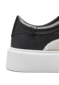 Black leather sneaker with a textured finish, featuring a white rubber sole. The design includes a contrasting light-colored fabric detail on the side.