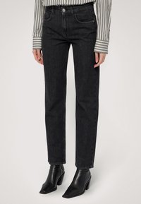 Jeans en denim noir taille haute avec une jambe droite, dotés de poches avant, de passants de ceinture et de détails de couture subtils. Associés à des bottines noires.