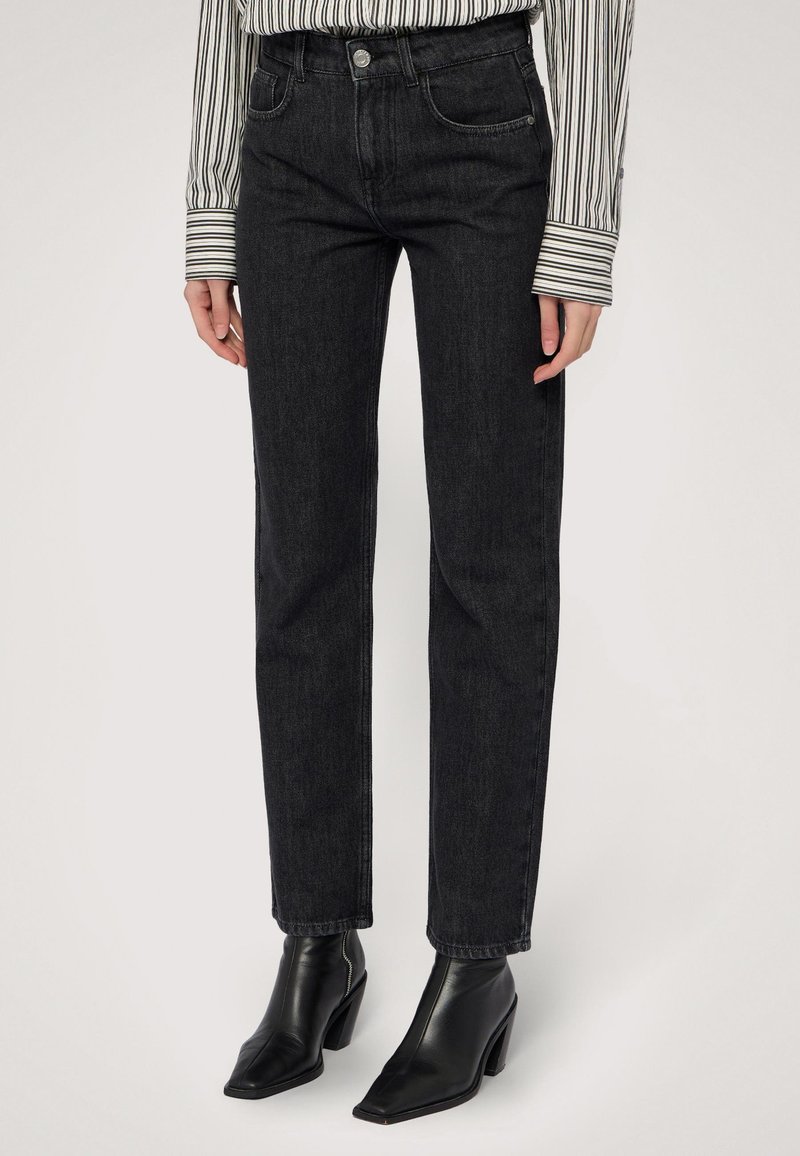 Jeans en denim noir taille haute avec une jambe droite, dotés de poches avant, de passants de ceinture et de détails de couture subtils. Associés à des bottines noires.