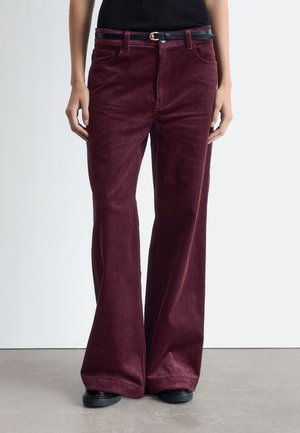 Burgundy corduroy flared pants with a textured finish. Features front pockets and a black belt with a gold buckle.