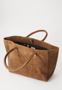 Bruine suède tote bag met twee handvatten, voorzien van een groot open compartment en een ritsvak aan de binnenzijde. Geïnt imprimeerd logo aan de zijkant.