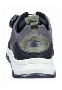 Grijze en zwarte sneaker met een textuur op de achterkant, voorzien van een cirkelvormig logo, een verstelbare knop en een contrasterende witte zool.