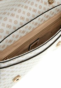 Borsa bianca con hardware dorato e un motivo a logo ripetuto. L'interno presenta una tasca con zip e una fodera liscia beige.