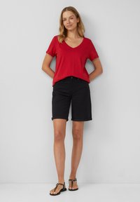 T-shirt rouge en v, shorts en denim noir avec des manches retroussées, sandales plates noires. Design simple avec un ajustement décontracté et confortable.