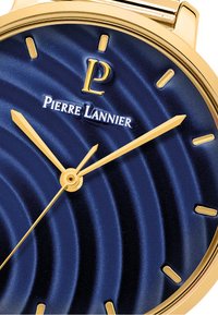 Guldtonad klocka med en texturerad, djupblå urtavla med vågmönster, guldtimmar och visare. Varumärket "Pierre Lannier" visas.
