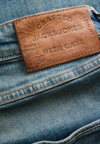 Smeđi kožni pečat s natpisom "Crafted Jack & Jones with care" urezan na struku plavih traperica.
