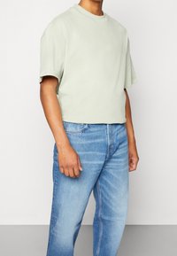 T-shirt verde chiaro a maniche corte con colletto rotondo, abbinato a jeans dritti di un leggero blu, leggermente consumati.