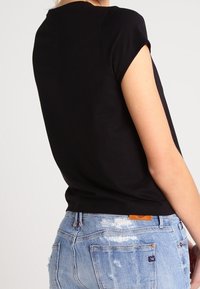 Osoba v černém krátkém rukávu a světle modrých roztrhaných džínech, zobrazená zezadu v úrovni pasu a ramen.