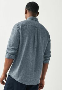 Camisa de manga larga para hombre en azul claro, de tejido texturizado con cuello abotonado y puños enrollados. Cuenta con un pliegue central en la parte posterior y un dobladillo curvado.