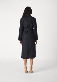 Navy striped shirt dress with long sleeves, belted waist, and mid-calf length, featuring a tailored collar and buttoned cuffs.