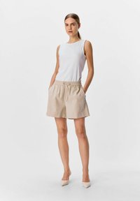 Pantaloni corti in cotone beige con vita elastica e cordoncino. Abbinati a una maglietta bianca senza maniche. Texture liscia, design casual.
