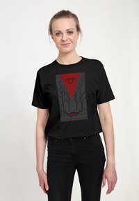 Černé tričko s krátkým rukávem s grafickým designem v červené a šedé barvě, zobrazením stromů a trojúhelníkového tvaru označeného jako "TWIN PEAKS."