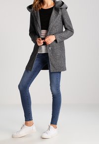 Grå, huva jacka med en texturerad finish, långa ärmar och dragkedja fram; ihop med blå slim jeans och vita sneakers.