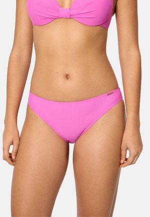 Mujer con un conjunto de bikini rosa brillante que muestra el abdomen y la parte superior de las piernas contra un fondo claro y liso.