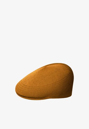 Berretto piatto giallo senape lavorato a maglia con motivi strutturati, cima arrotondata e visiera corta, mostrato su sfondo bianco.