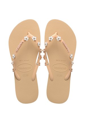 Peach-colored flip-flops with floral embellishments, textured rubber sole, and contrasting straps featuring silver beads and flower accents.