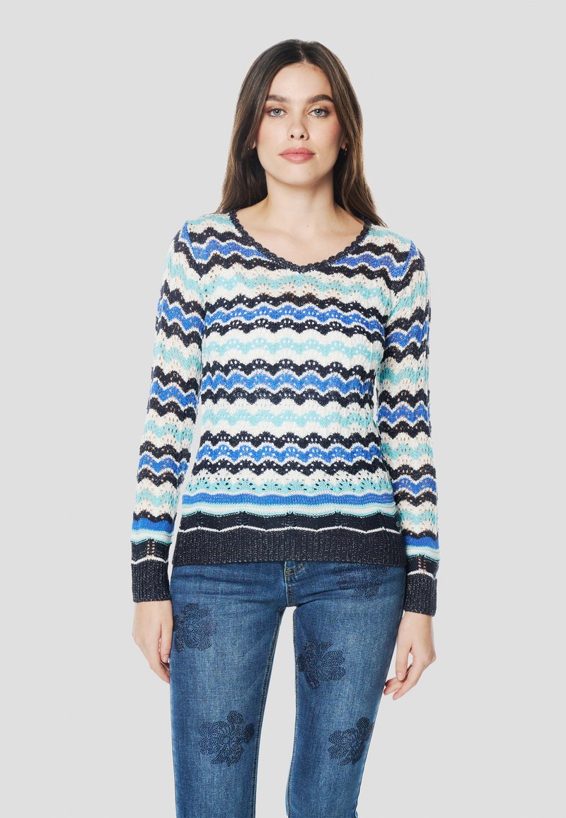 Kötött pulóver hullámos mintával kék, fehér és fekete színekben. Hosszú ujjú, kerek nyakkivágással. Farmernadrággal párosítva.