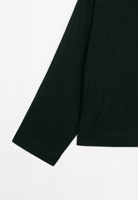 Black long-sleeve top with a textured fabric, featuring a pocket and a straight hem. The sleeves have a relaxed fit and a folded cuff.