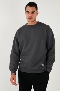 Sudadera gris oscuro con escote redondo, manga larga y puños acanalados. Presenta una pequeña etiqueta de la marca en la parte inferior izquierda. Textura suave.