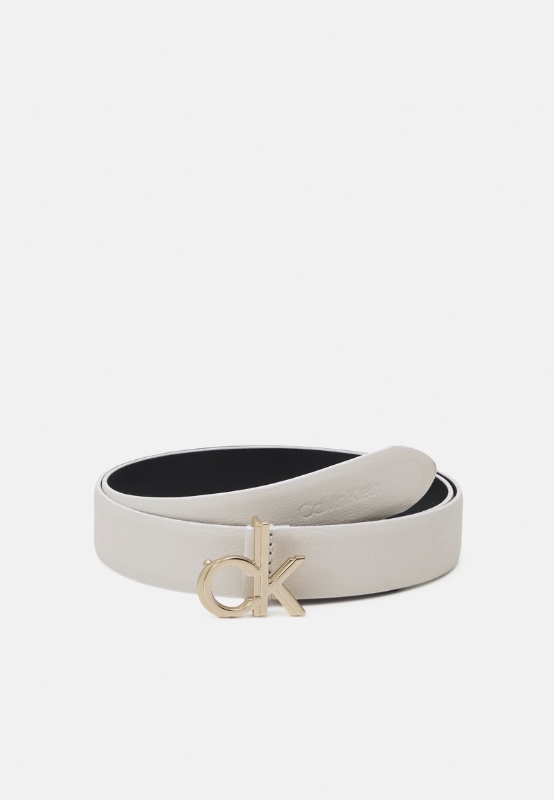 Ceinture en cuir blanc enroulée avec une boucle à logo "ck" dorée, présentant une texture lisse et une doublure intérieure noire sur un fond uni.