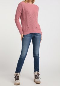 Růžový pletený svetr s texturovaným vzorem, kulatým výstřihem a žebrovanými manžetami. Nosený s tmavě modrými džíny a béžovými botami s kožešinovým lemováním.