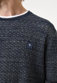 Navy Strickpullover mit strukturiertem Muster, weißem Rundhalsausschnitt und kleinem Markenlogo-Patch auf der linken Brust.