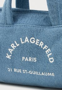 Saco de lona em denim azul claro com texto branco que diz "KARL LAGERFELD PARIS 21 RUE ST-GUILLAUME" curvado na parte da frente e no topo.