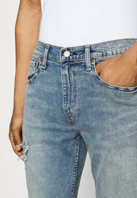 Ljusblå denimjeans med hög midja, med framfickor, knappstängning och slitna detaljer vid låret.