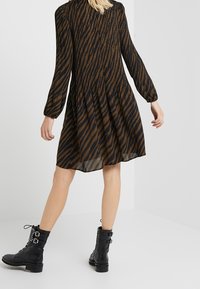 Brun- och svartrandig klänning med långa ärmar, en samlad midja och en flödande silhuett, tillsammans med svarta snörade ankelstövlar.