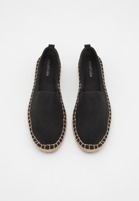 Espadrilles en toile noire avec une semelle en jute, à enfilage, et des détails de couture contrastants autour du bord.