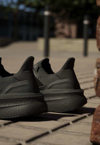 Двойка черни маратонки Adidas Ultraboost на осветена от слънцето павирана повърхност на открито с размит фон.