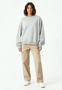 Felpa grigia oversize con polsini a coste, abbinata a pantaloni cargo color khaki con tasche laterali e sneakers bianche. Design semplice.