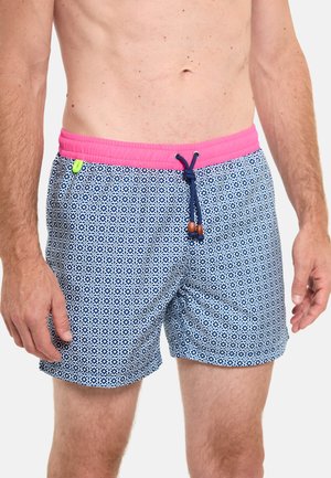 Homme portant un short de bain bleu et blanc à motifs avec une ceinture rose et un cordon bleu marine, debout les bras détendus le long du corps.