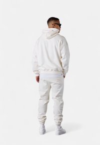 Sweatshirt à capuche blanche et joggers en tissu doux. Présente une coupe décontractée avec des bords rib et un petit détail de marque près de la taille.