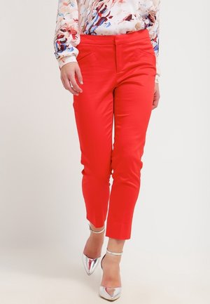 Rode op maat gemaakte broek met een gladde textuur, cropped pasvorm en zijzakken. Gekoppeld aan glanzende zilveren hakken en een blouse met een meerkleurig patroon.