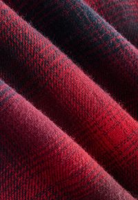 Țesătură din amestec de lână în nuanțe de roșu, cu un model negru de houndstooth. Textura este moale, cu fibre vizibile și țesătură diagonală.