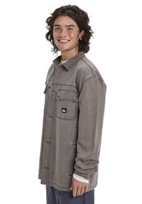 Graue Denimjacke mit Knopfleiste, zwei Brusttaschen und einem Logo-Patch. Mit langen Ärmeln und einer lockeren Passform.