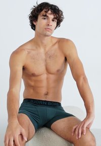 Sötétzöld boxernadrág fekete "BJÖRN BORG" derékpánttal, rugalmas anyagból készült, testhez simuló kialakítással, amely kiemeli a test vonalait.