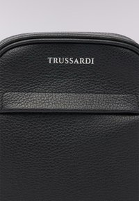 Zaino in pelle nera con una finitura testurizzata. Caratterizzato da un design elegante, logo argento "TRUSSARDI" e una tasca frontale embossata.