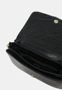 Sac en cuir noir avec une finition texturée, doté d'une fermeture à pression dorée et de poches zippées intérieures pour une meilleure organisation.