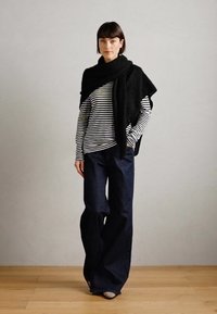 Sort oversize sweater lagt over en sort og hvid stribet langærmet top, vidde bukser i mørkeblå, og lyse sko.