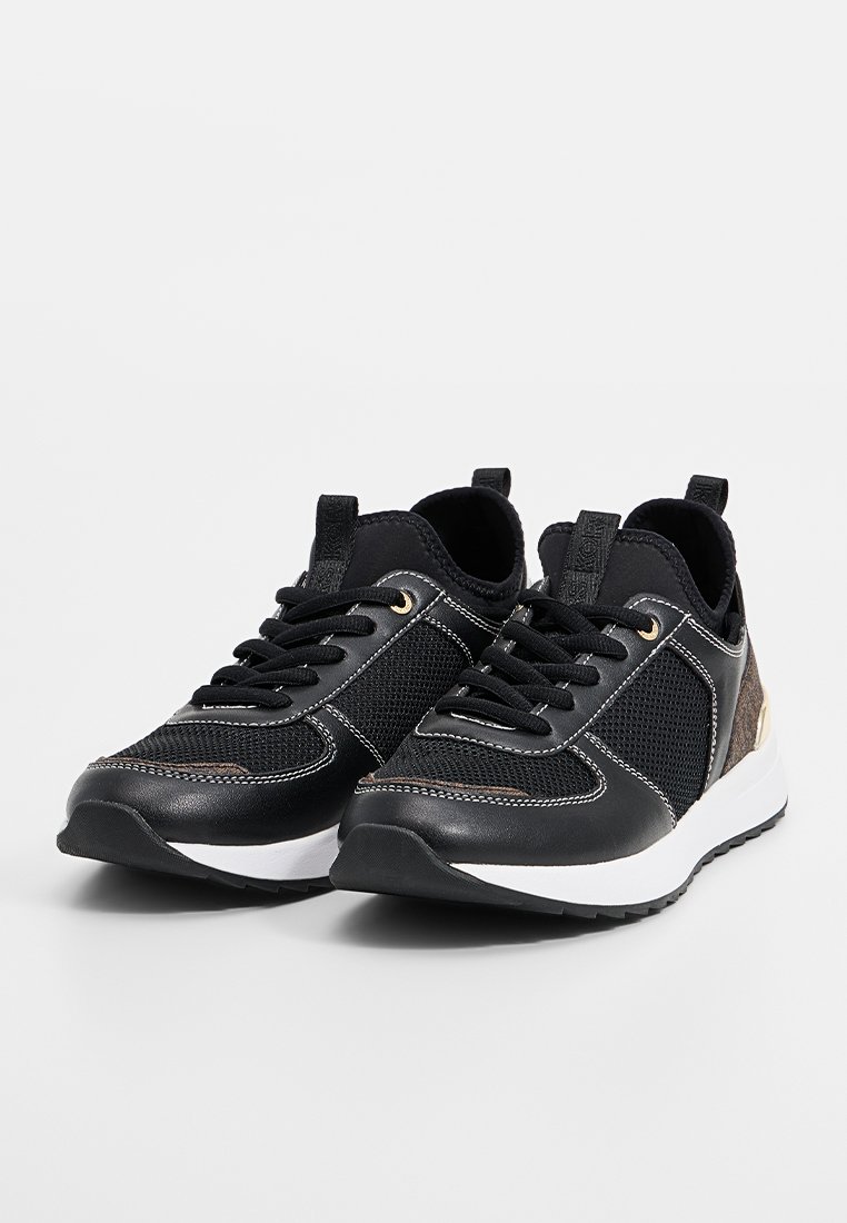 Par de zapatillas deportivas negras con suelas blancas, detalles de malla y cuero, cordones negros y tiradores sobre una superficie blanca.