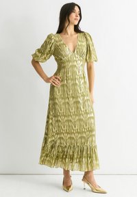 Green maxi dress with a subtle pattern, puff sleeves, V-neck, and a flared ruffled hem. Paired with metallic pointed-toe heels.