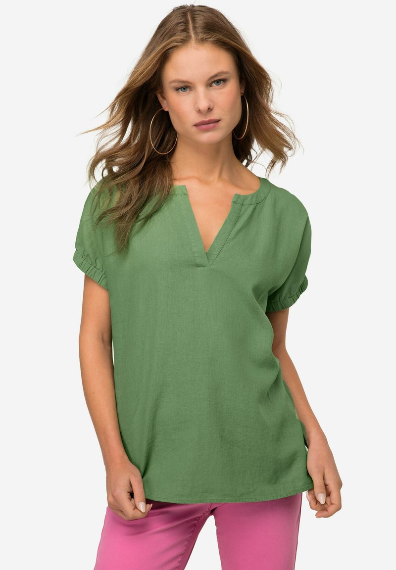 Top verde in lino a maniche corte con scollo a V e maniche arricciate, abbinato a pantaloni rosa. Texture liscia e vestibilità comoda.