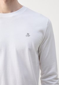 Hvid langærmet t-shirt lavet af bomuld med rund hals. Har et lille, gråt broderet "M OP" logo på brystet.