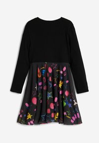 Langärmliges Kleid mit schwarzem Oberteil und einem bunten, bedruckten Rock mit Sternen und abstrakten Mustern, aus weichem Stoff gefertigt.